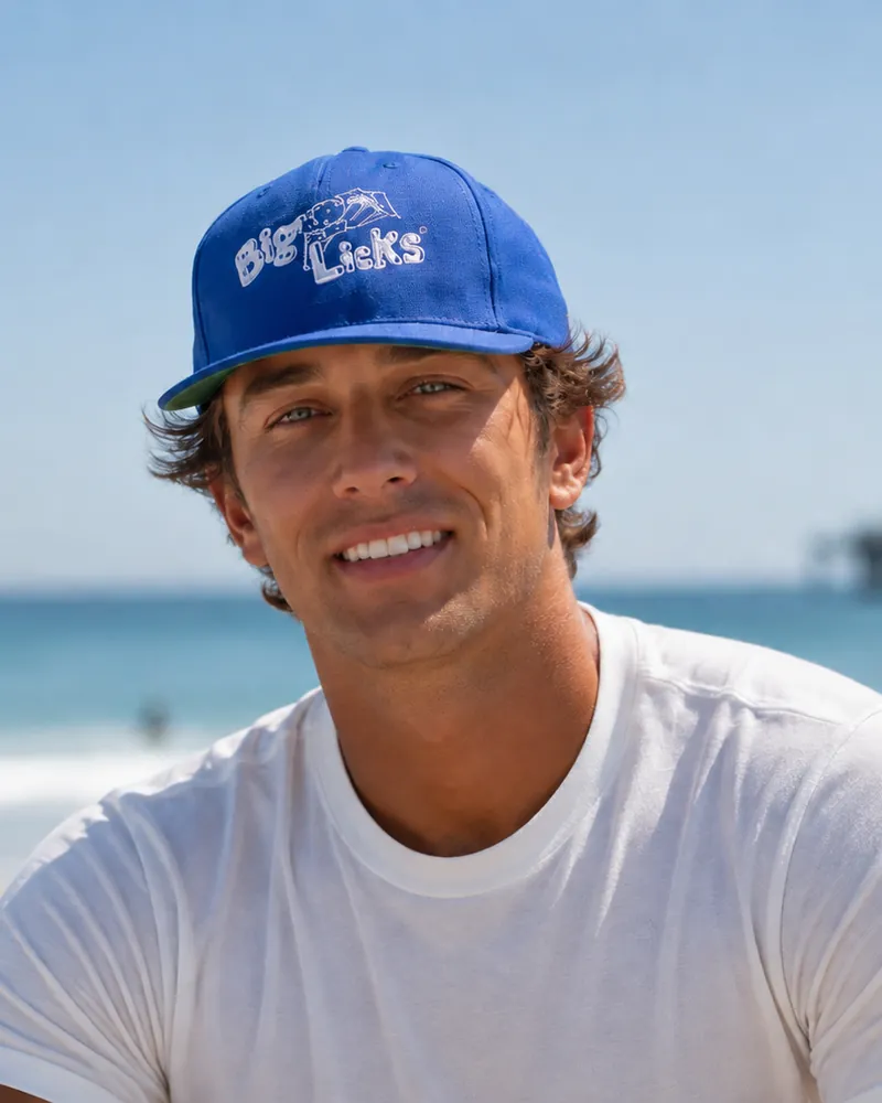 A man wearing the royal blue Big Licks cap on the beach